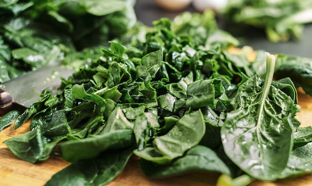 Saftige grüne geschnittene spinatblätter liegen auf einem holzbrett. selektiver fokus, nahaufnahme von spinat. die idee, das frühstück aus gesunden bio-lebensmitteln zuzubereiten