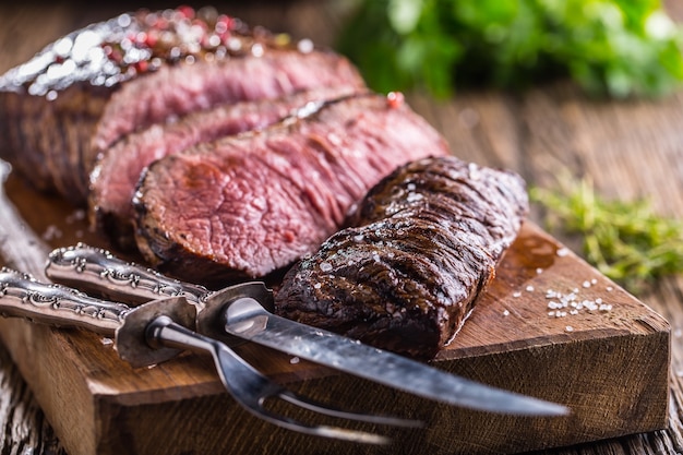 Saftige mittelgroße rib-eye-steakscheiben vom rind auf holzbrett mit gabel- und messerkräutern, gewürzen und salz