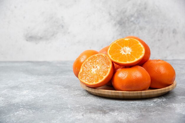 Saftige Orangenfrüchte mit Scheiben in einem Holzteller auf Steintisch.