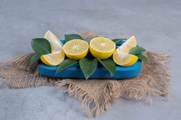 Saftige Zitronenscheiben und Blätter auf einer blauen Platte auf Marmorhintergrund.
