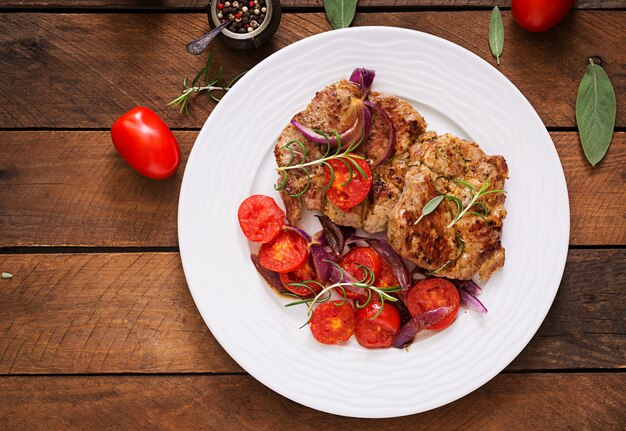 Saftiges Schweinefleischsteak mit Rosmarin und Tomaten auf einer weißen Platte