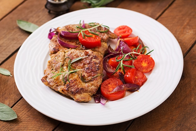 Saftiges Schweinefleischsteak mit Rosmarin und Tomaten auf einer weißen Platte