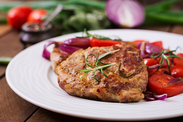 Kostenloses Foto saftiges schweinefleischsteak mit rosmarin und tomaten auf einer weißen platte