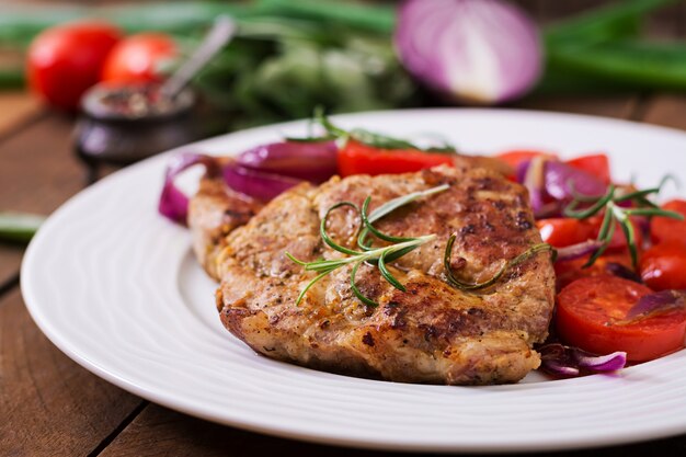 Saftiges Schweinefleischsteak mit Rosmarin und Tomaten auf einer weißen Platte