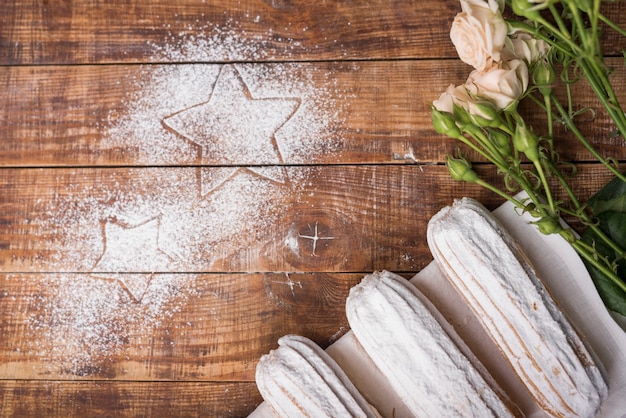 Sahnige gebackene eclairs mit rosa rosen mit den sternen gezeichnet auf zuckerpulver über dem hölzernen schreibtisch