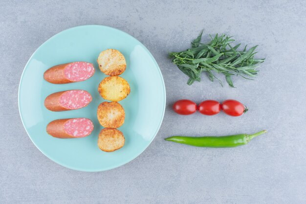 Salami mit Bratkartoffeln auf blauem Teller mit Gemüse.