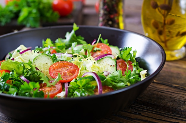 Salat aus Tomaten, Gurken, roten Zwiebeln und Salatblättern. Gesundes Sommer-Vitamin-Menü. Vegane Gemüsenahrung. Vegetarischer Esstisch.