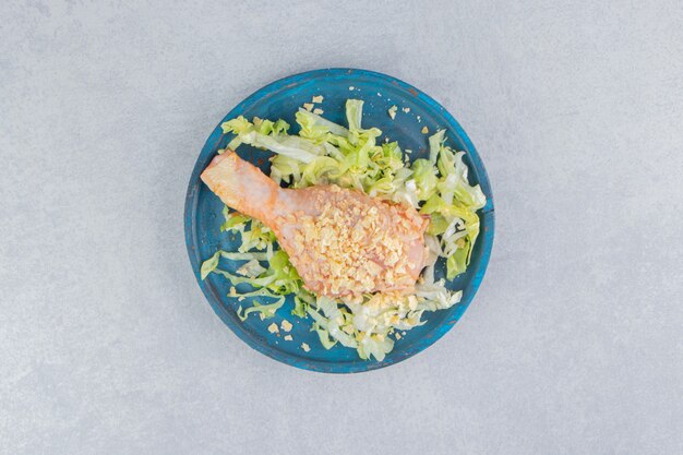 Salat und Hähnchenschenkel in der Holzplatte, auf der blauen Oberfläche