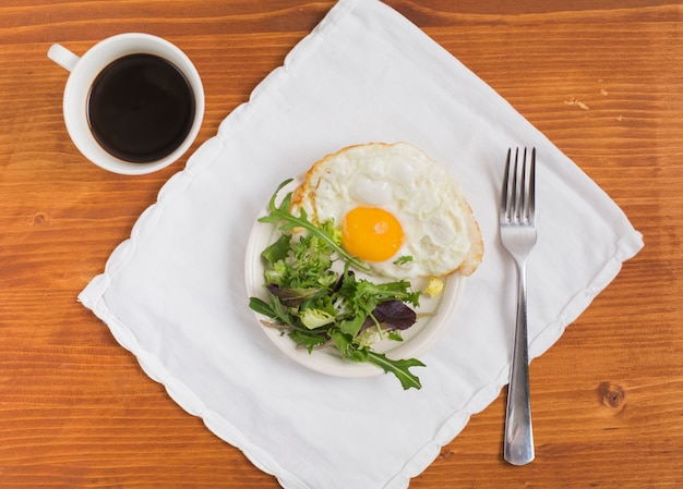 Kostenloses Foto salat und halber spiegelei auf platte über der serviette mit tasse tee