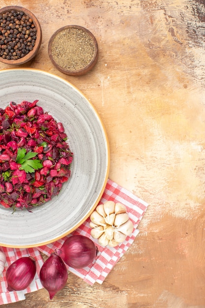 Salat von oben auf einem grauen Teller mit schwarzem Pfeffer gemahlener schwarzer Pfeffer oben und roten Zwiebeln Knoblauch unten auf einem hölzernen Hintergrund mit Kopienplatz