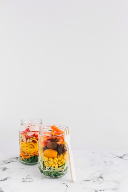 Kostenloses Foto salatgemüse in zwei weckglas mit gabel gegen weißen hintergrund