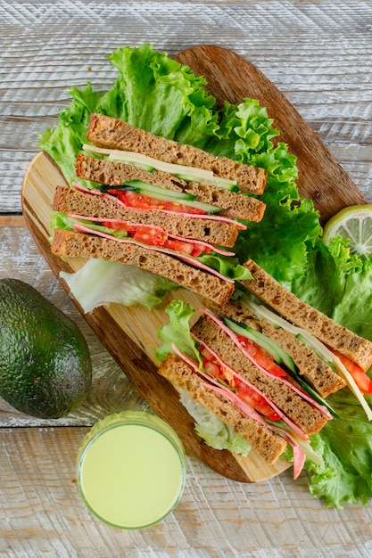 Sandwich mit Käse, Schinken, Saft, Avocado flach auf Holz und Schneidebrett liegen