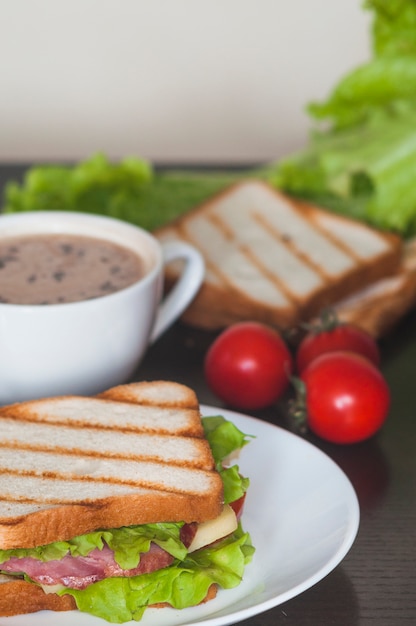 Sandwich mit Schinken; Spinatblatt und -käse auf weißer Platte mit Kaffee