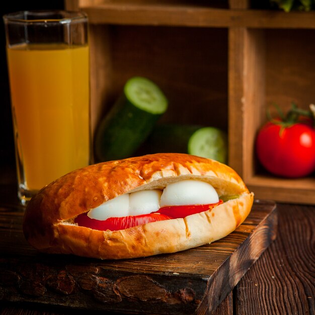 Sandwich mit Tomaten und Käse mit Orangensaft und Gurken in Holzbrett