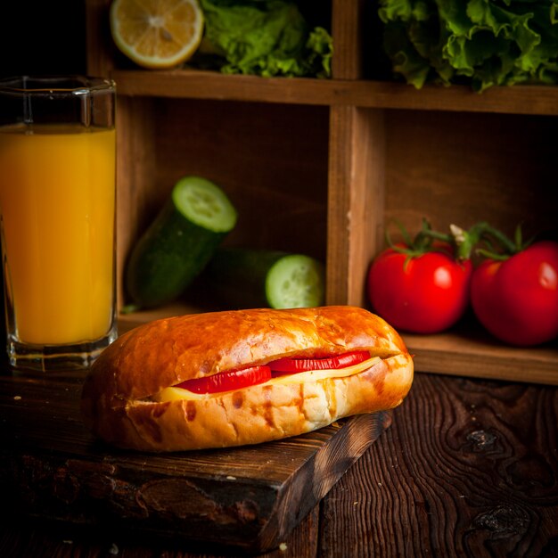Sandwich mit Tomaten und Käse mit Orangensaft und Gurken und Salat in Holzbrett
