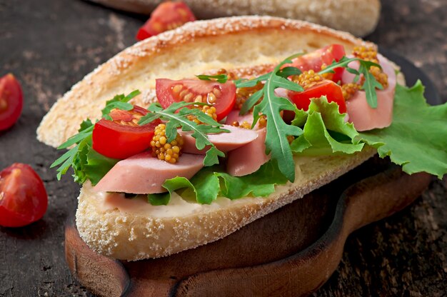 Sandwich mit Wurst, Kopfsalat, Tomate und Arugula auf der alten Holzoberfläche