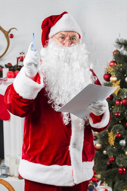 Sankt, die mit Papier nahe verziertem Weihnachtsbaum steht