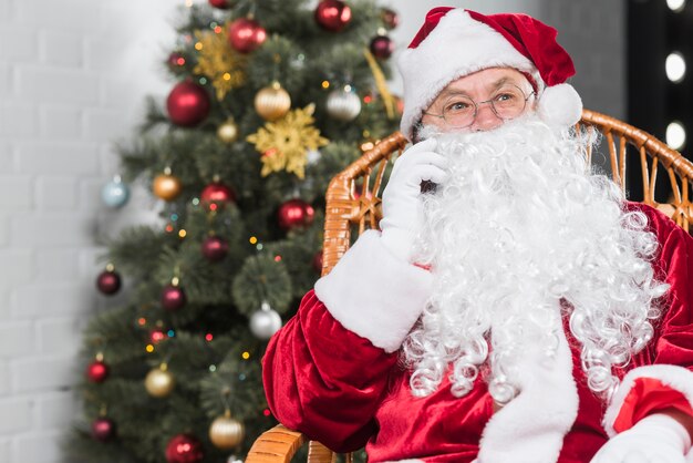 Santa Claus, die auf Stuhl sitzt und telefonisch spricht