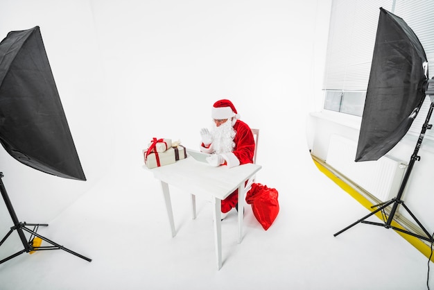 Kostenloses Foto santa claus, die bei tisch im fotostudio sitzt