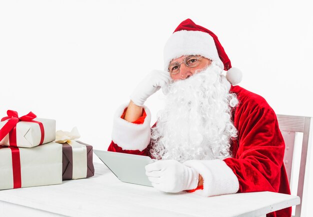 Santa Claus, die bei Tisch mit Tablette sitzt