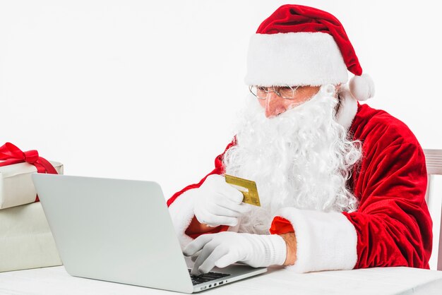 Santa Claus, die mit Laptop und Kreditkarte sitzt