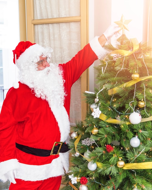 Santa Claus, die Stern auf Weihnachtstannenbaum setzt