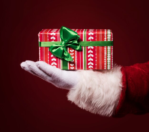 Santa Claus Hände halten eine Geschenkbox auf rotem Hintergrund