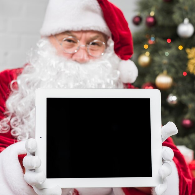 Santa Claus in den Gläsern, die Tablette in den Händen halten
