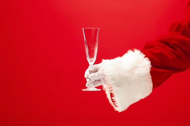 Santa Holding Champagner Weinglas über rotem Hintergrund. Die Jahreszeit, Winter, Feiertag, Feier, Geschenkkonzept
