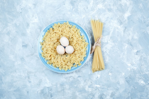 Satz Eier, Spaghetti und Farfalle-Nudeln in einem Teller auf einem Gipshintergrund. flach liegen.