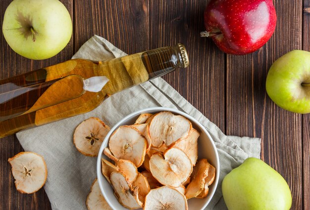 Satz frischer Apfel und Saft und getrocknete Äpfel in einer Schüssel auf einem Tuch und hölzernem Hintergrund. Draufsicht.