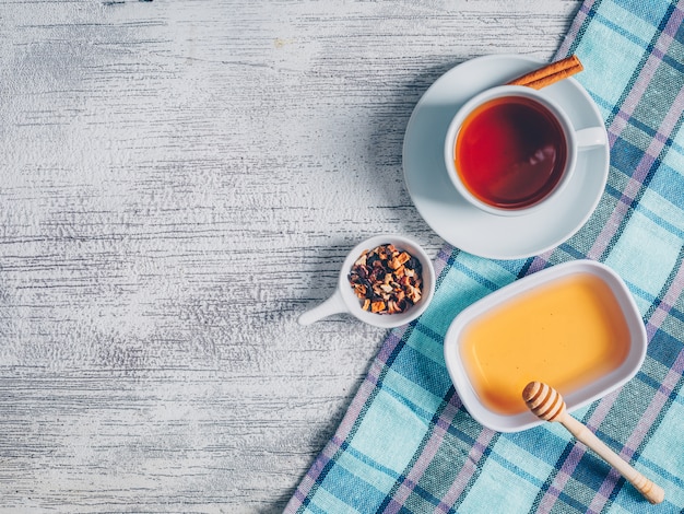 Satz Honig und Tee Kräuter und eine Tasse Tee auf einem Picknicktuch und grauem Holzhintergrund. Draufsicht. Platz für Text