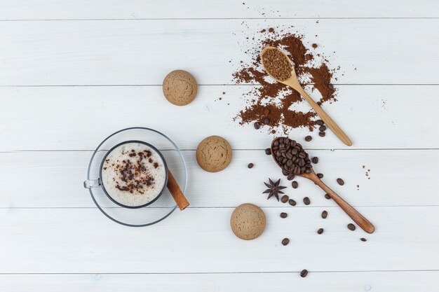 Satz Kekse, gemahlener Kaffee, Kaffeebohnen, Zimtstange und Kaffee in einer Tasse auf einem hölzernen Hintergrund. flach liegen.