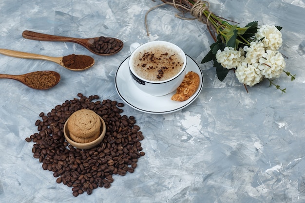 Satz kekse, kaffeebohnen, gemahlener kaffee, blumen und kaffee in der tasse auf einem grungy grauen hintergrund. high angle view.