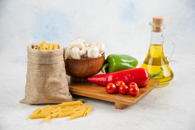 Satz Pilze, natives Olivenöl extra, Nudeln, Kirschtomaten und Chilischoten auf einem Stück Marmor.