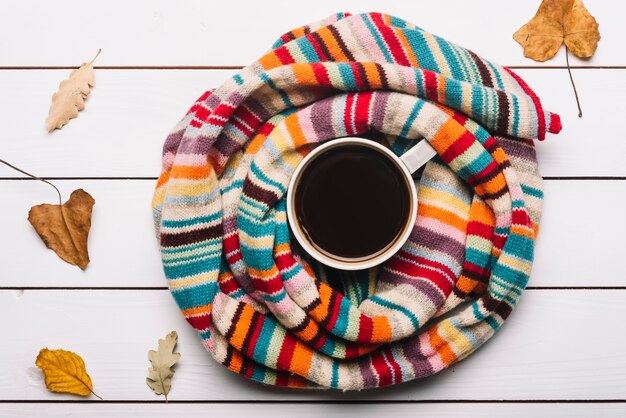 Schal und Herbstlaub, die um Kaffee liegen