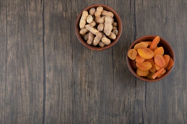 Schalen mit gesunden getrockneten Aprikosenfrüchten und Erdnüssen in der Schale auf einem Holztisch.