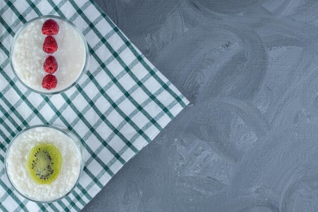 Schalen mit milchigem Reis, garniert mit Himbeeren und Kiwi-Scheibe auf einer Tischdecke auf Marmorhintergrund.