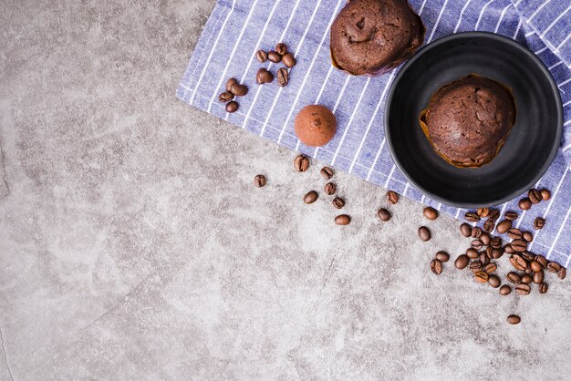 Schalenkuchen und Röstkaffeebohnen auf Serviette über dem konkreten Hintergrund