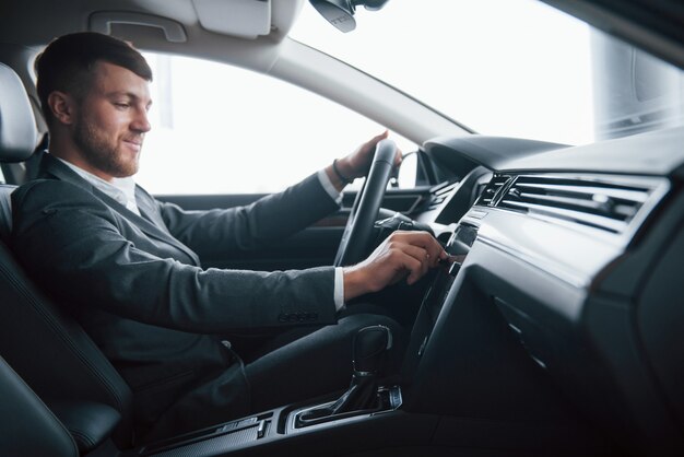 Schalten Sie die Musik ein. Moderner Geschäftsmann, der sein neues Auto im Autosalon versucht