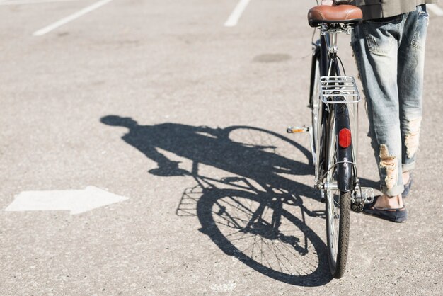 Schatten des Mannes gehend mit Fahrrad auf Asphalt