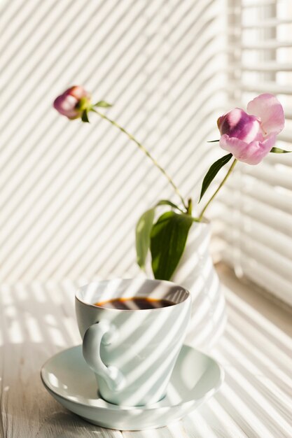 Schatten von Jalousien auf Kaffeetasse und Blumenvase