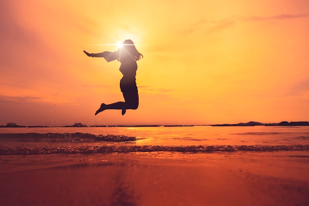 Schattenbild der asiatischen jugendlich frau, die auf sonnenuntergangstrandfreiheitsideenkonzept springt