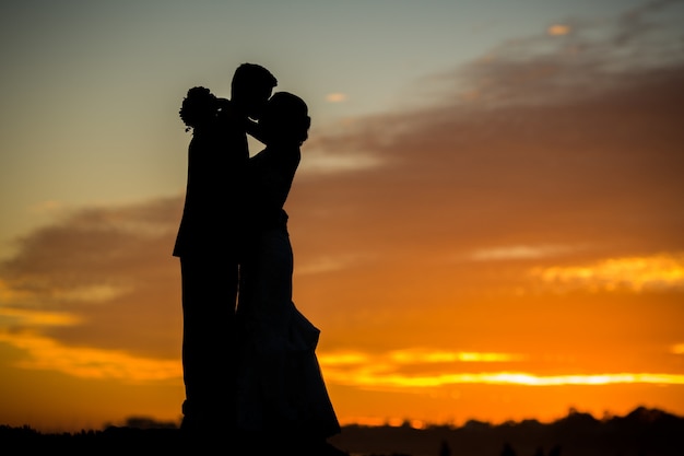 Schattenbild der Braut und des Bräutigams, die während Sonnenuntergang küssen