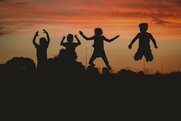 Schattenbild der Kinder, die auf dem Hügel posieren, umgeben von Grün während eines goldenen Sonnenuntergangs