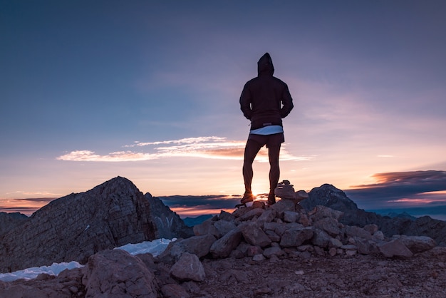 Schattenbild der Person stehend auf den Felsen, die Sonnenuntergang aufpassen