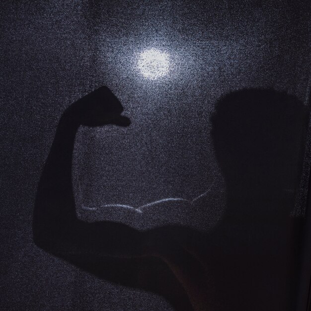 Schattenbild des anonymen Mannes, der Muskeln biegt