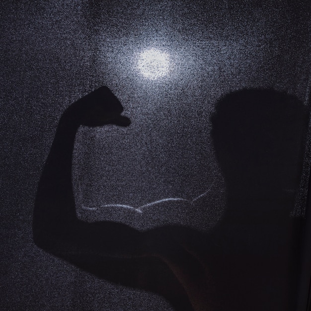 Schattenbild des anonymen Mannes, der Muskeln biegt