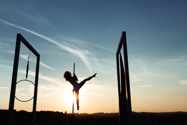 Schattenbild des sexy Pfostentänzers, der am Dach bei Sonnenuntergang durchführt