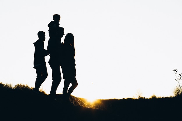 Schattenbild einer Familie, die durch die Sonnenuntergangzeit geht